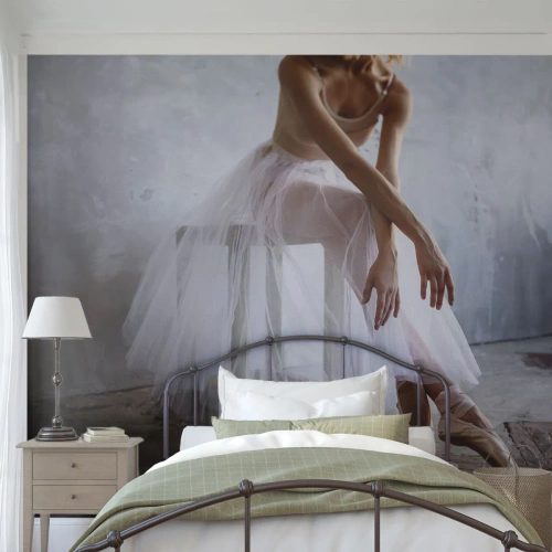 Fototapet Standard Eco - En ballerina som vilar i baletttofflor mot en industriell bakgrund. - 100x70cm - Innan rampljuset tänds - Modern väggdekoration för vardagsrum och sovrum ARTTOR